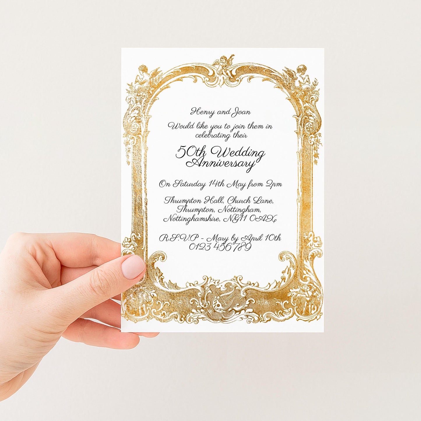 a hand holding a wedding invitation card with an ornate gold frame.