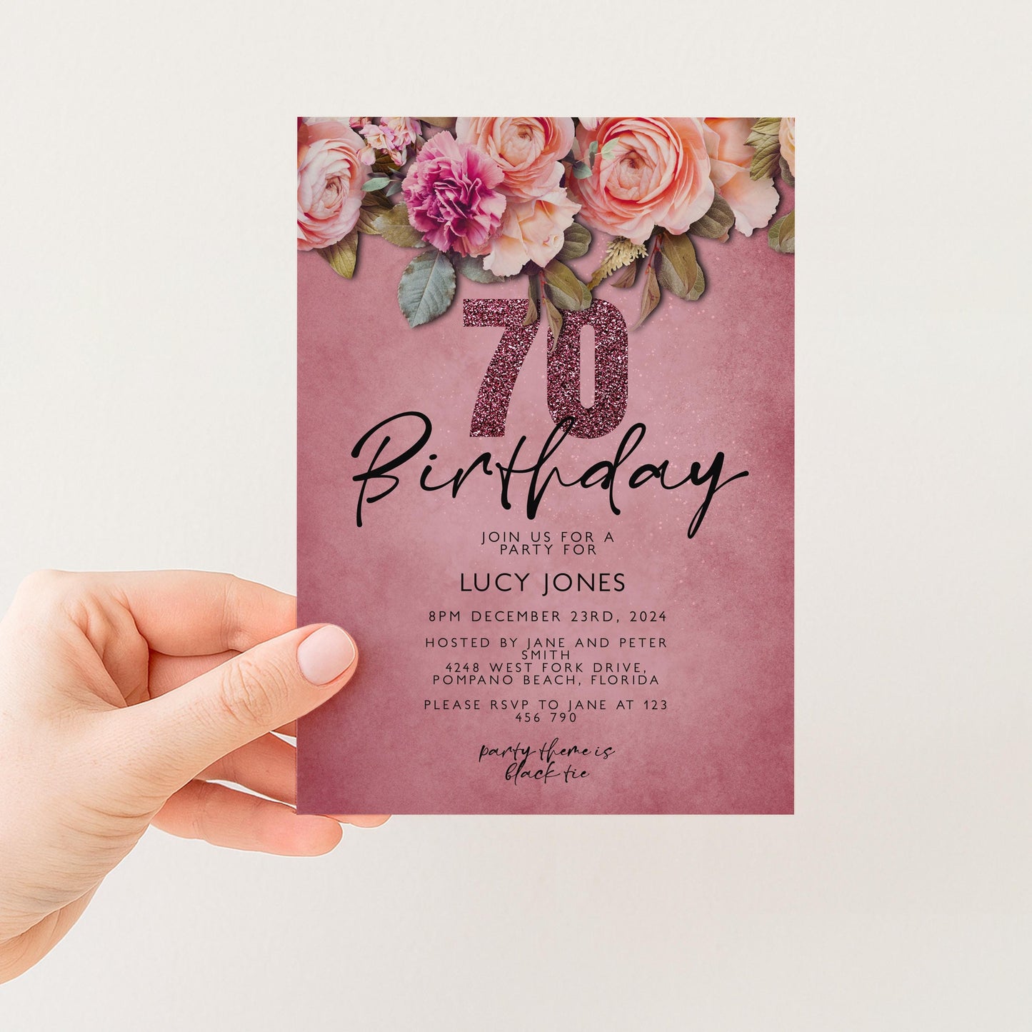 A hand holding a pink birthday invitation card with a floral design and the number 70 on it.