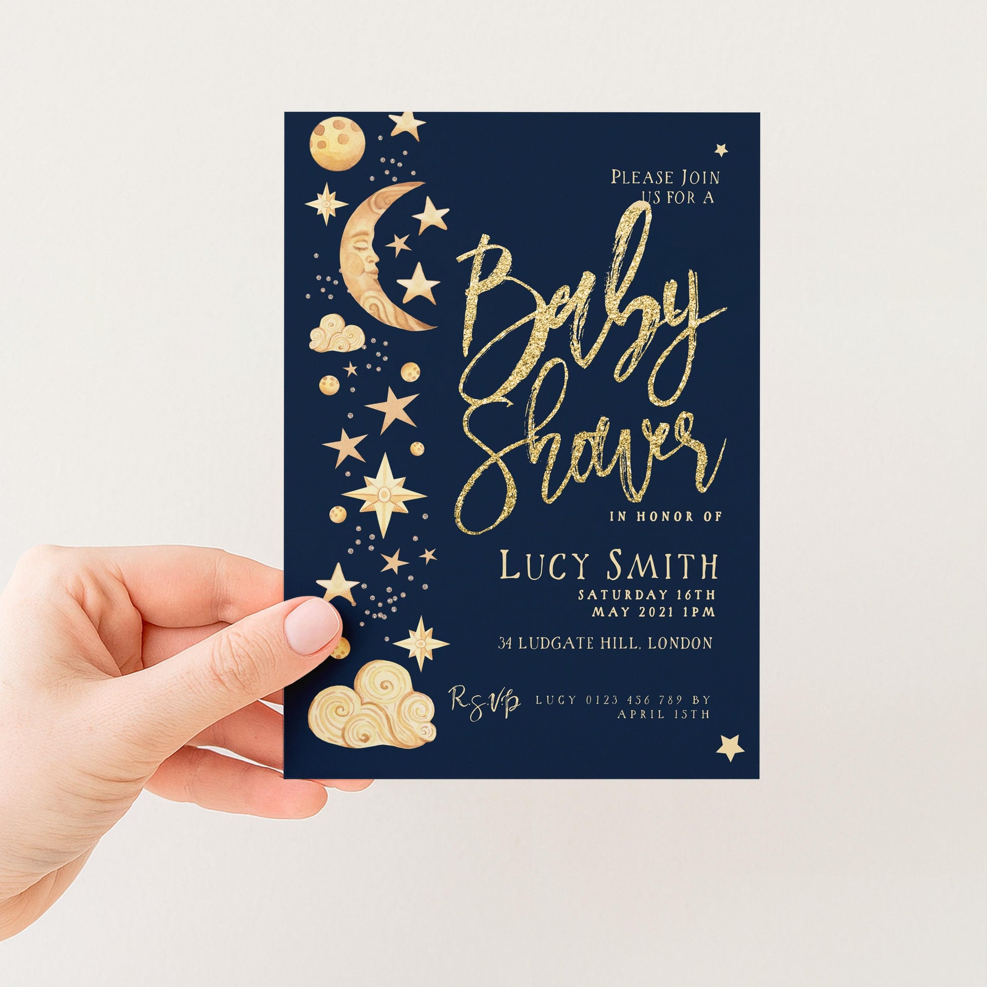 a hand holding a blue invitation card with gold stars and a crescent moon design. The card is for a baby shower event, and it invites guests to join the celebration in honor of Lucy Smith.