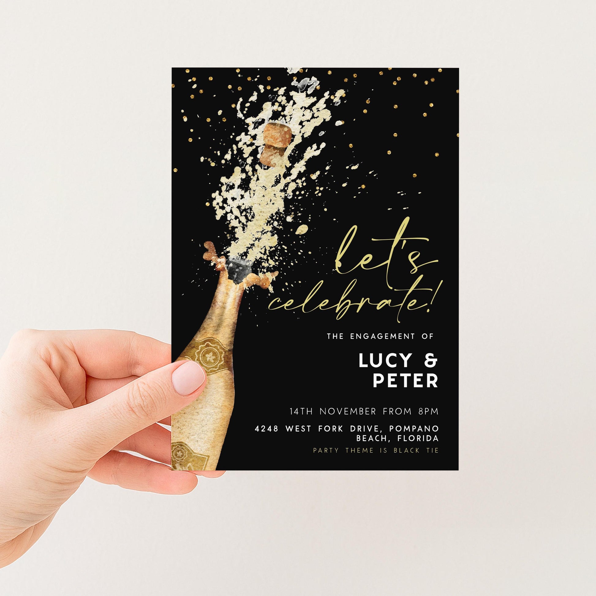 A hand holding a black and gold invitation card with a champagne bottle and a celebratory splash of champagne.