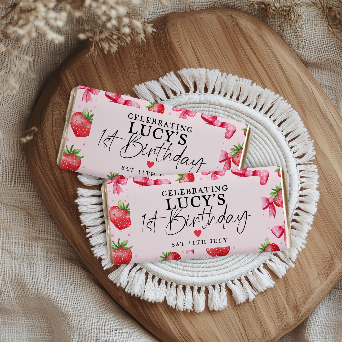 Editable pink strawberry chocolate bar wrapper with red berries and bows, personalized for a 1st birthday party, displayed with festive holiday decor.