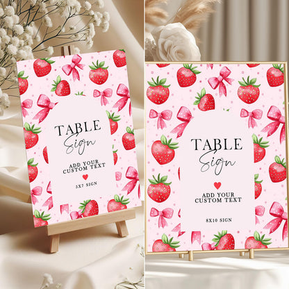 Editable strawberry-themed table signs in 5x7 and 8x10 sizes with pink background, red strawberries, and bows, displayed on mini easels for birthday party decor.