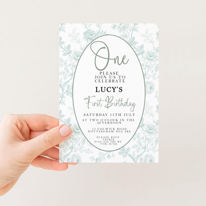 a person holding a white invitation card with a floral design. The card is for a first birthday celebration and invites guests to join in the festivities.