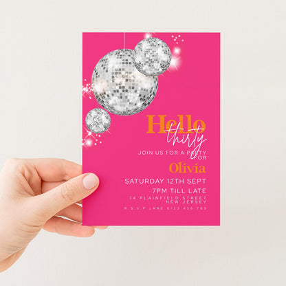 A hand holding a pink invitation card with disco balls and text.