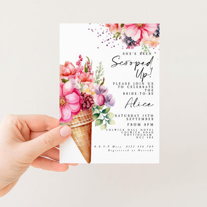 A hand holding a white invitation card with a floral design and text.