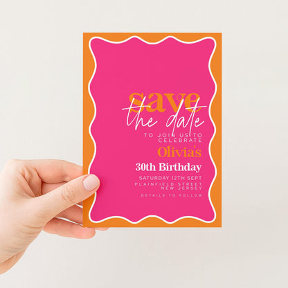 a person's hand holding a pink and orange wedding invitation card.