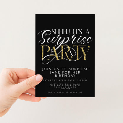 a hand holding a black and gold invitation card with text and details about a surprise party.
