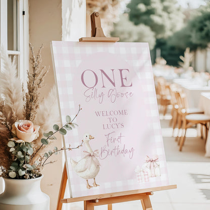 Pink silly goose birthday welcome sign with gingham background and goose illustration, displayed on easel at outdoor 1st birthday party