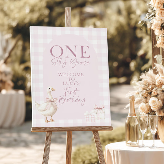 Pink silly goose birthday welcome sign with gingham background and goose illustration, displayed on easel at outdoor 1st birthday party