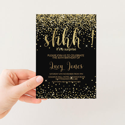 a hand holding a black and gold birthday invitation card with a glittery design.