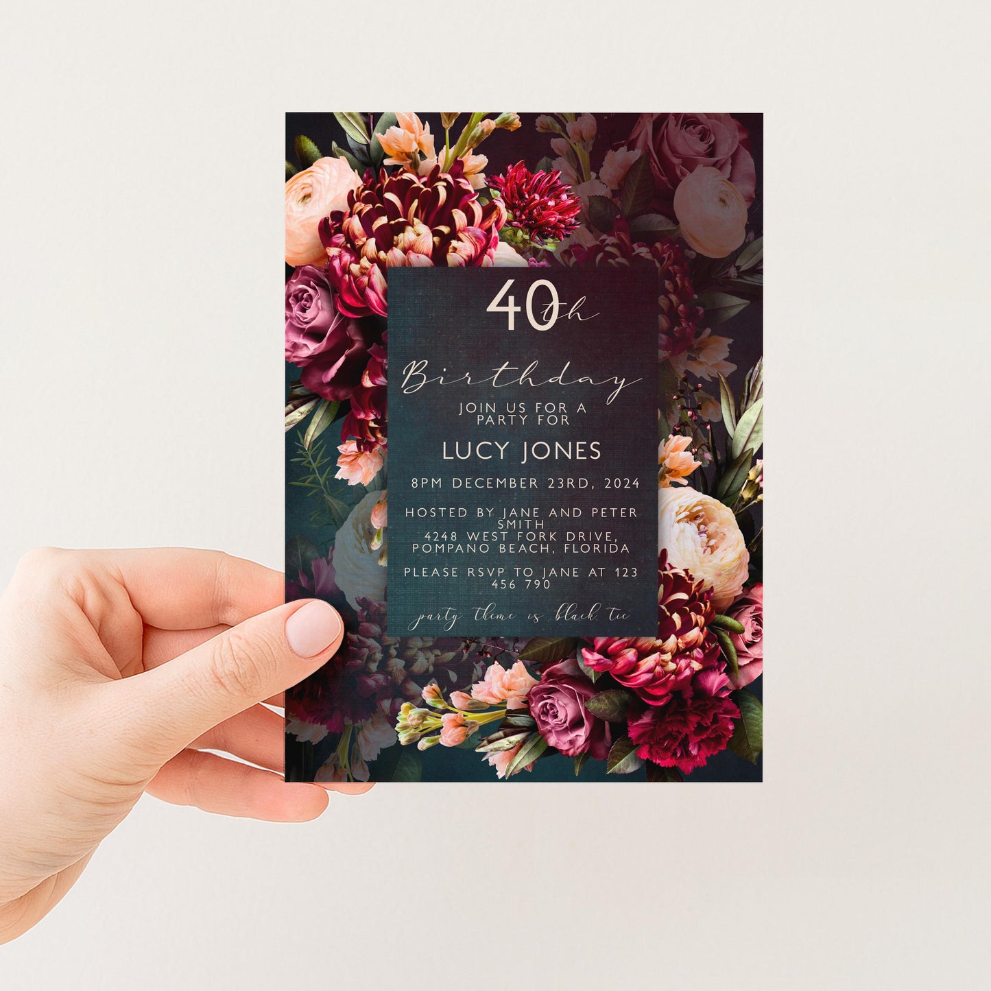 A hand holding a floral birthday invitation card with a dark background and a large floral design.