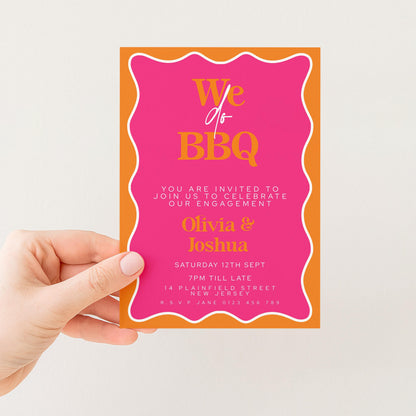 a hand holding a pink and orange invitation card with text and details about an event.