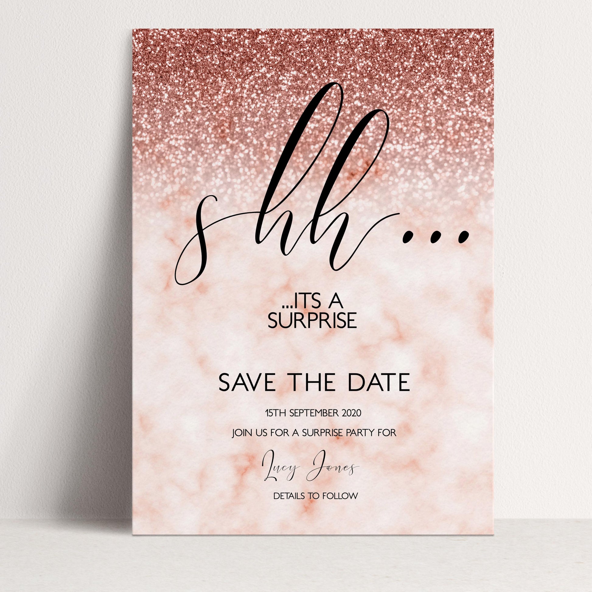 The image is a pink and gold glittery wedding invitation with the text "shh... it's a surprise" and "SAVE THE DATE" printed on it.