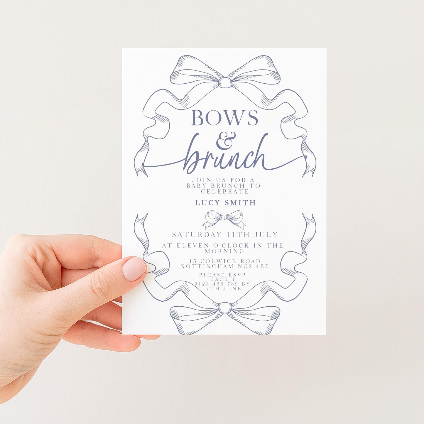 a hand holding a white invitation card with a decorative blue ribbon design. The card appears to be for a bridal shower, as indicated by the text and the event details provided.