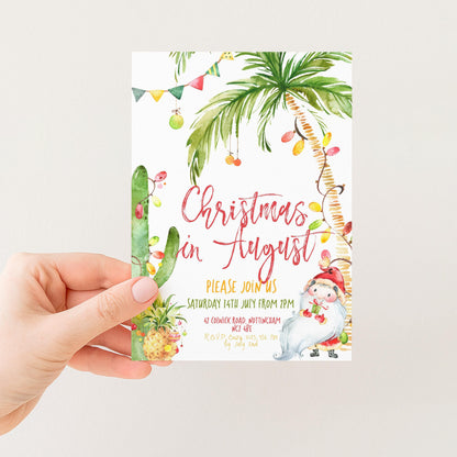 A hand holding a Christmas invitation card with a tropical theme, featuring palm trees, a cactus, and other festive decorations.