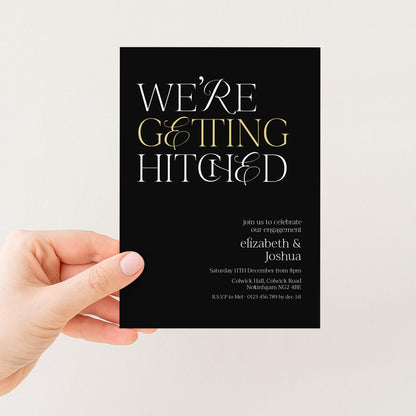 a hand holding a black wedding invitation card with white text.