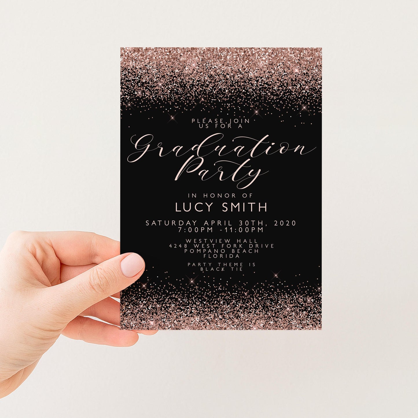 a hand holding a graduation party invitation card with a black background and a glittery gold border. The text on the invitation reads "Graduation Party in honor of Lucy Smith" and provides details about the event, including the date, time, location, and dress code.
