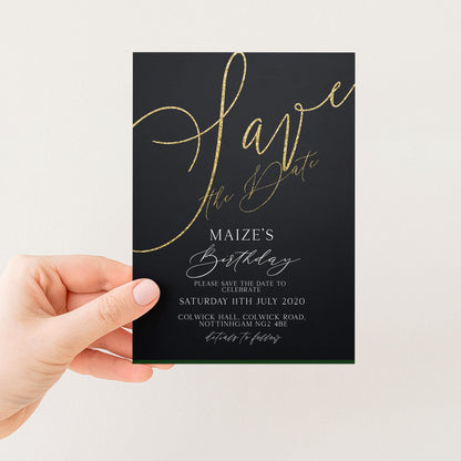 a hand holding a black wedding invitation card with gold text and details.