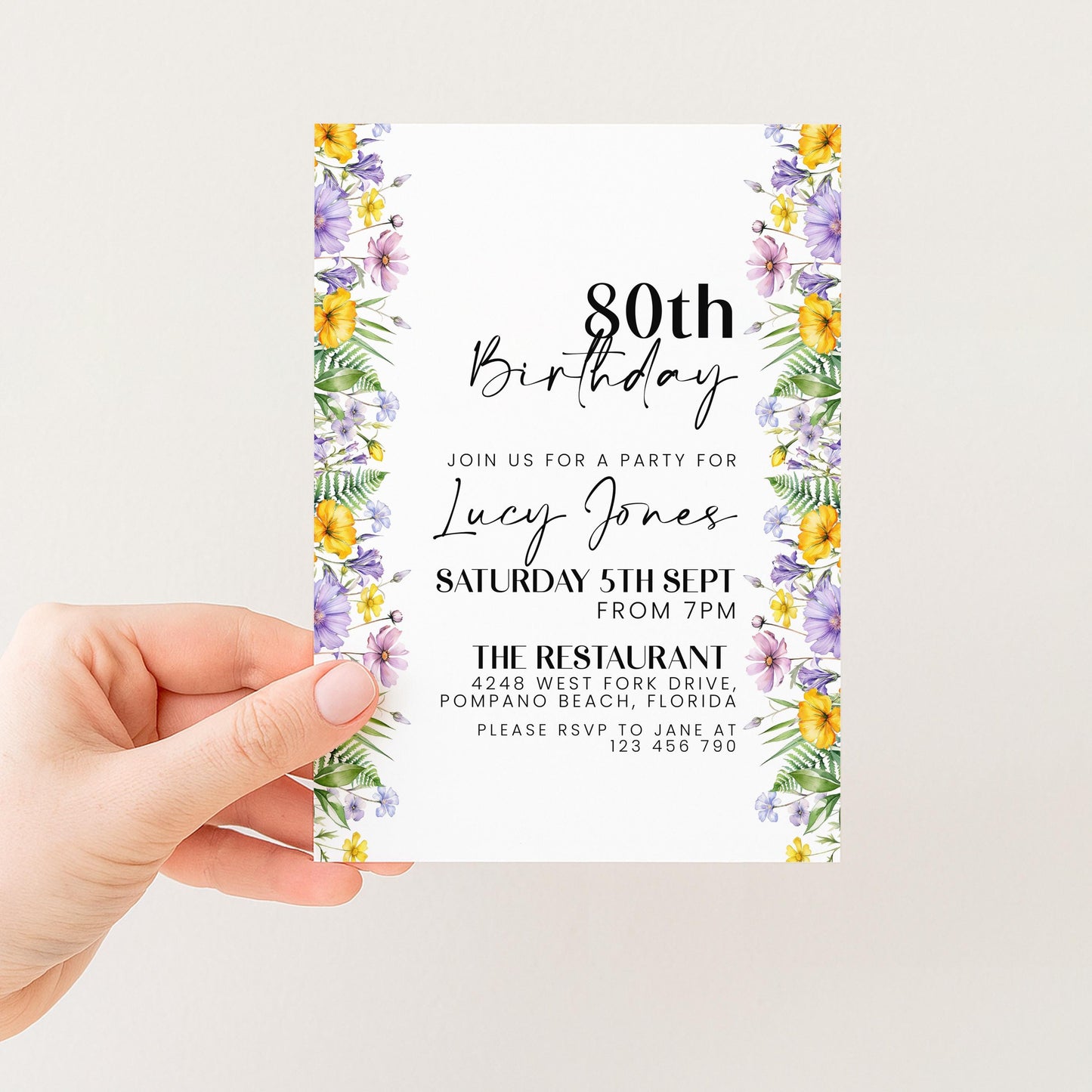 a person holding a birthday invitation card with a floral border. The card is designed for a birthday party for a woman named Lucy Jones, and it includes details about the event, such as the date, time, location, and RSVP information.