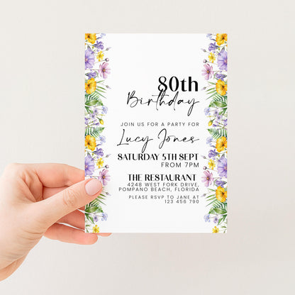 a person holding a birthday invitation card with a floral border. The card is designed for a birthday party for a woman named Lucy Jones, and it includes details about the event, such as the date, time, location, and RSVP information.