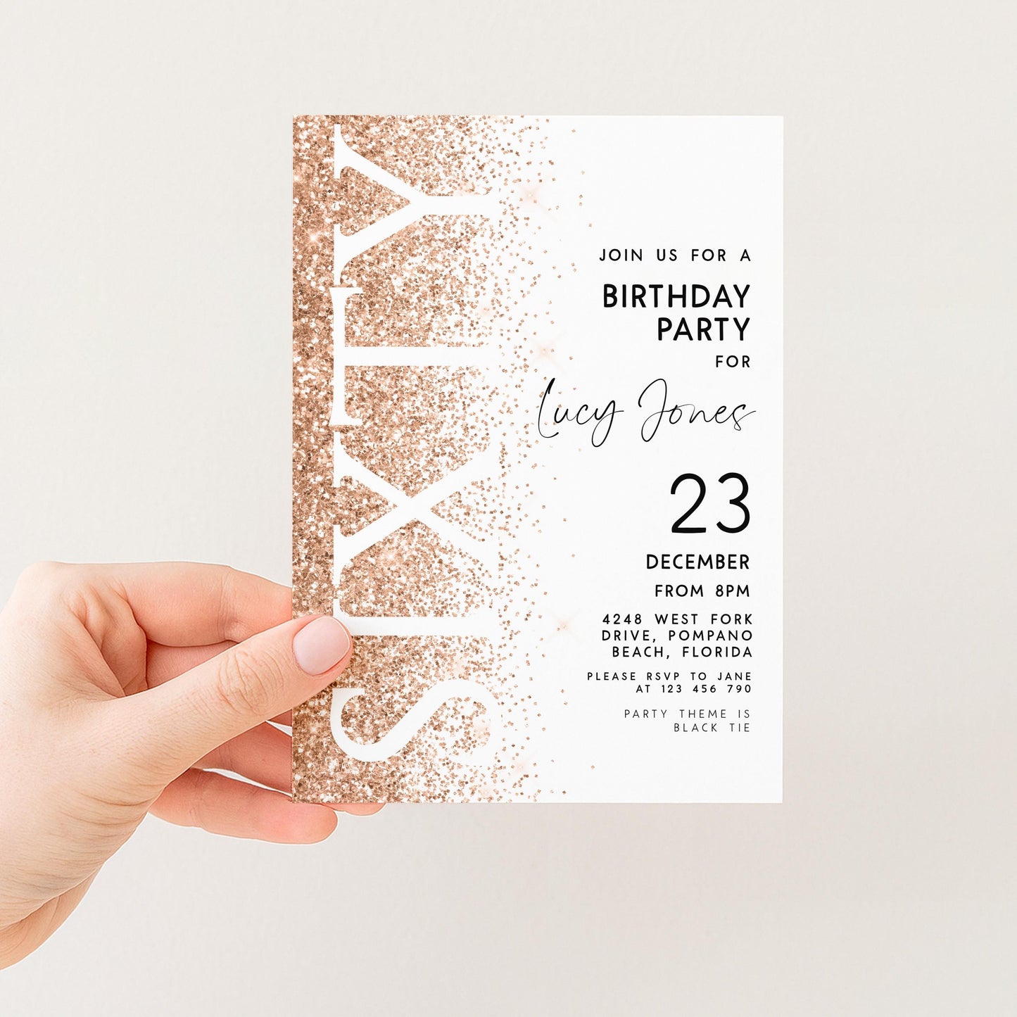 a person's hand holding a birthday party invitation card. The card has a gold glitter design and text inviting guests to a birthday party for a woman named Lucy Jones.
