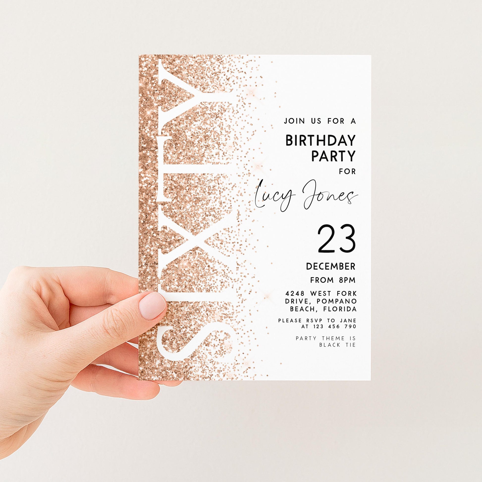 a person's hand holding a birthday party invitation card. The card has a gold glitter design and text inviting guests to a birthday party for a woman named Lucy Jones.