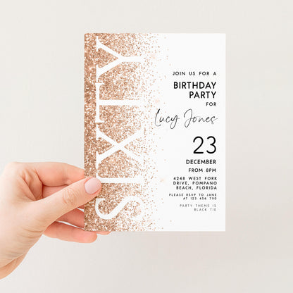 a person's hand holding a birthday party invitation card. The card has a gold glitter design and text inviting guests to a birthday party for a woman named Lucy Jones.