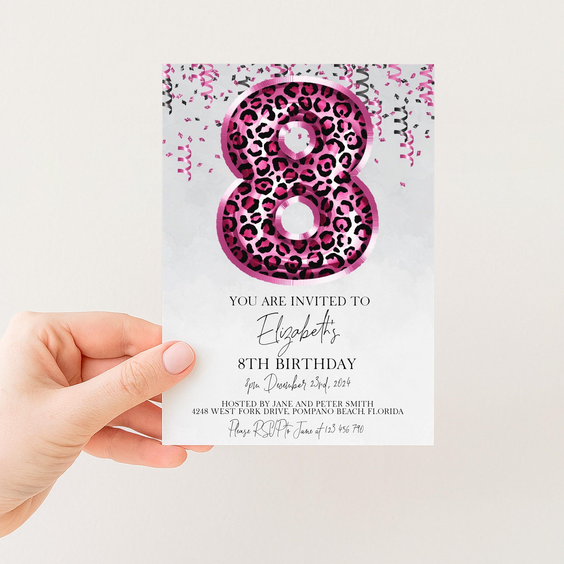 A hand holding a birthday invitation card with a large number 8 and pink and black leopard print design.