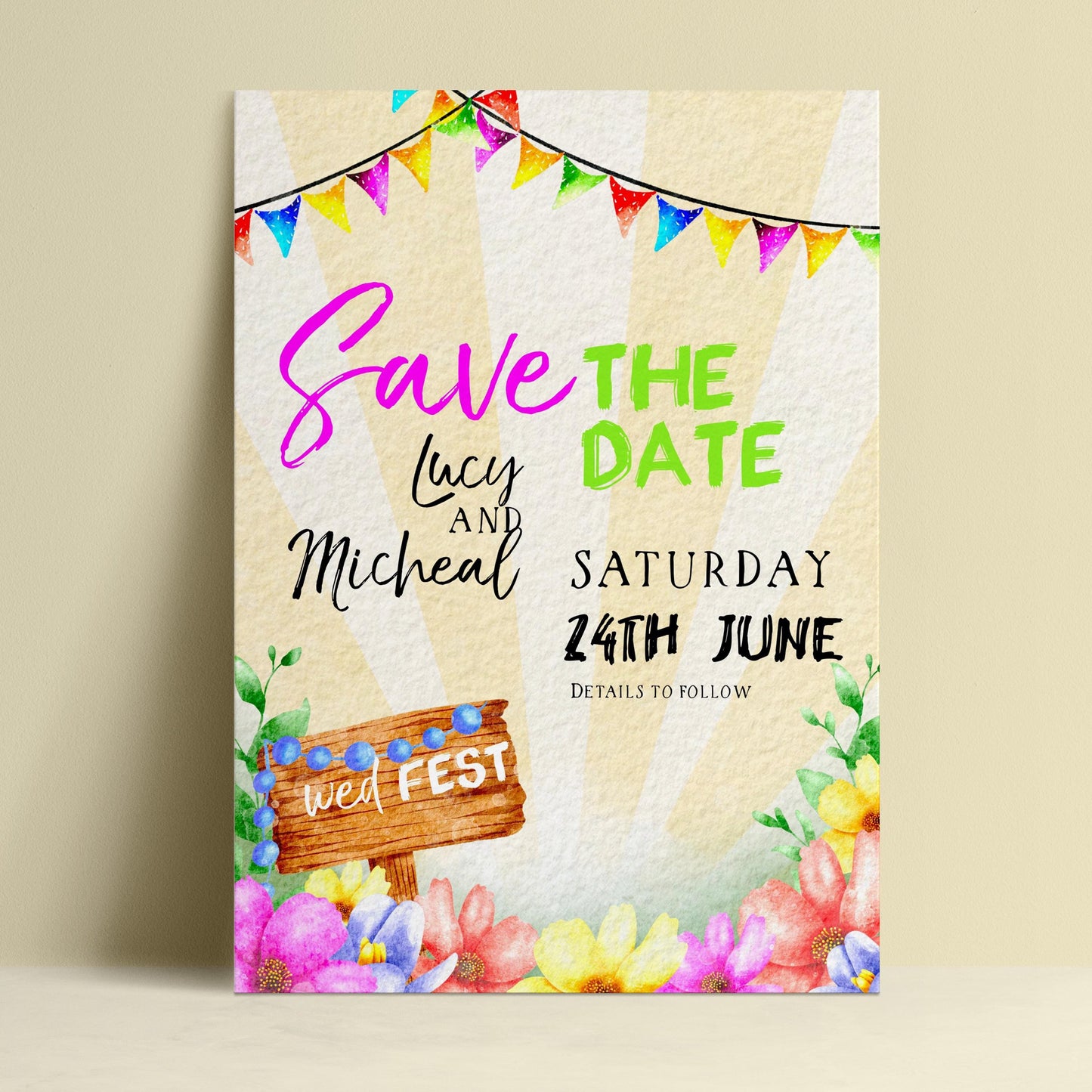 The image is a colorful wedding invitation featuring a wooden sign, flowers, and a string of multicolored flags.