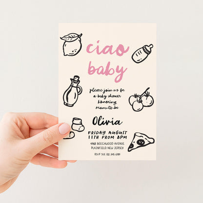 The image is a hand holding a baby shower invitation card with various baby-related illustrations and text.