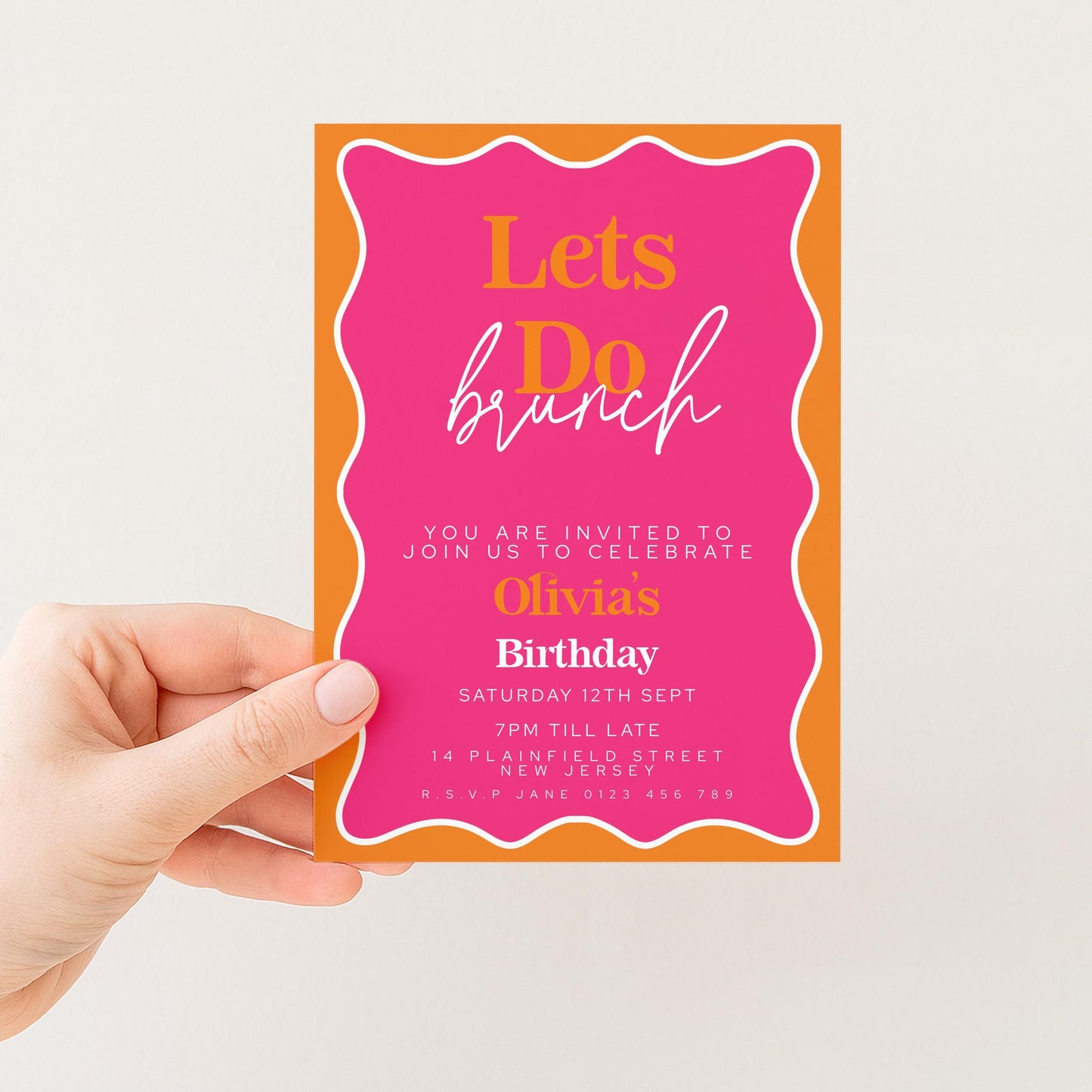 a person's hand holding a colorful birthday invitation card with a pink and orange background.