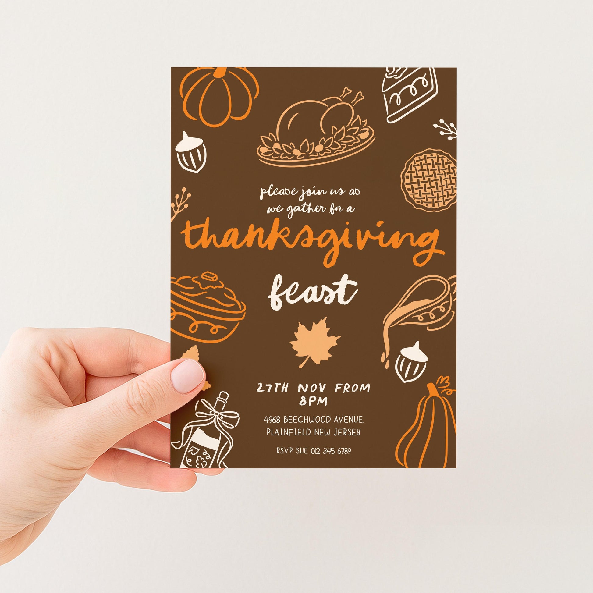 A hand holding a brown and orange Thanksgiving feast invitation card with various fall-themed illustrations and text.