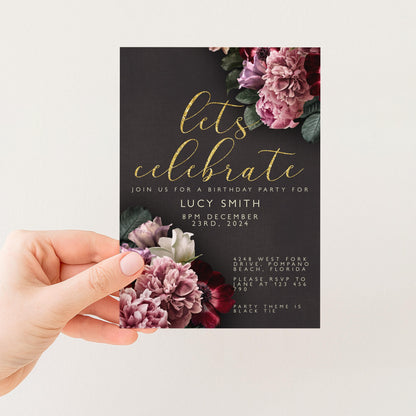 A hand holding a birthday party invitation card with a floral design.