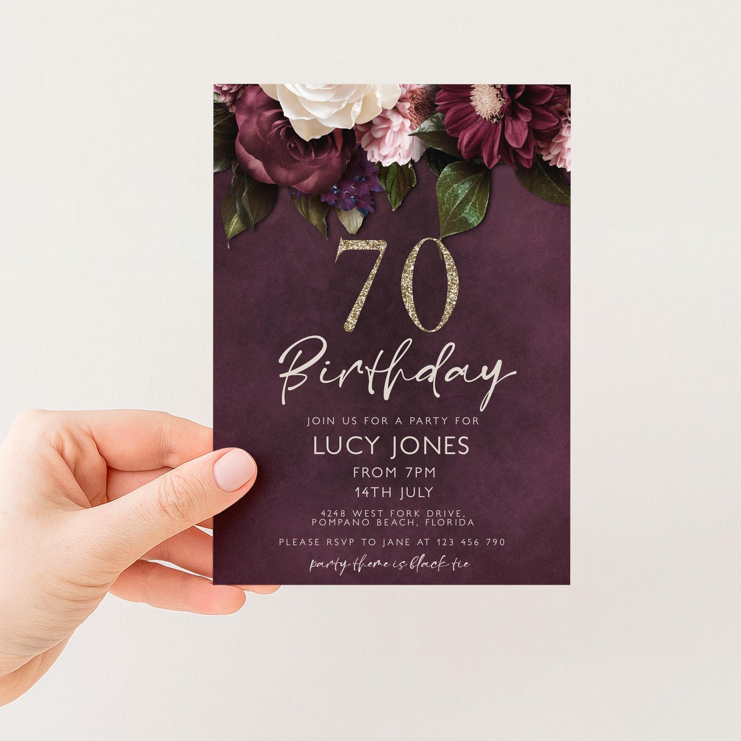 A hand holding a birthday invitation card with a floral design and the number 70 on it.