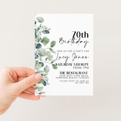 A hand holding a white invitation card with a green leaf design.