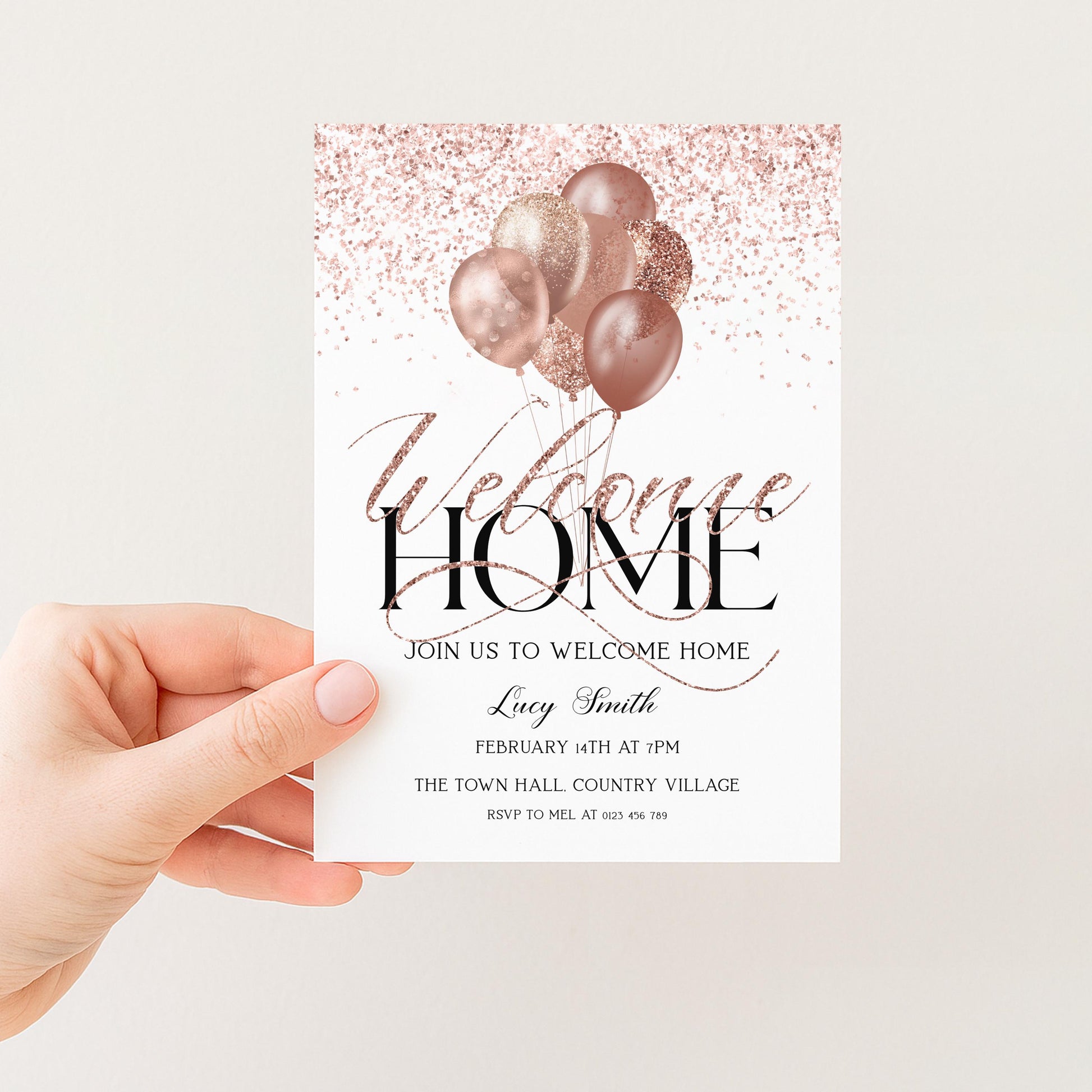 a person's hand holding a white invitation card with a pink and gold glitter design and the text "Welcome Home" written on it.