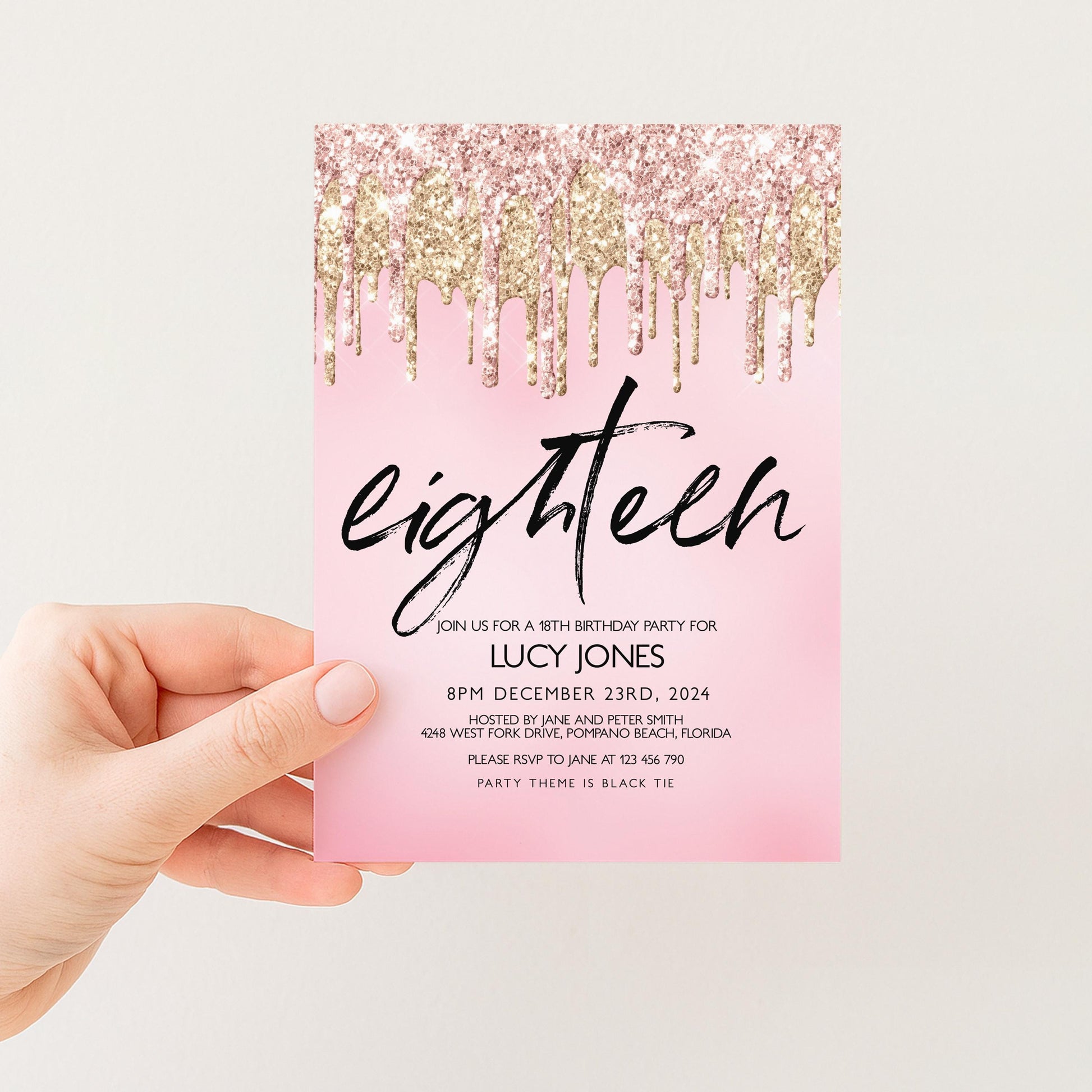 A hand holding a pink invitation card with a pink background and gold glitter drizzle.