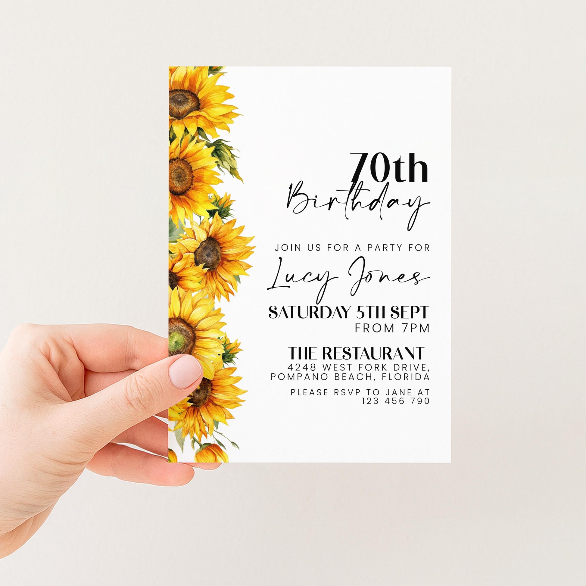 a hand holding a birthday invitation card with a floral design featuring yellow sunflowers.