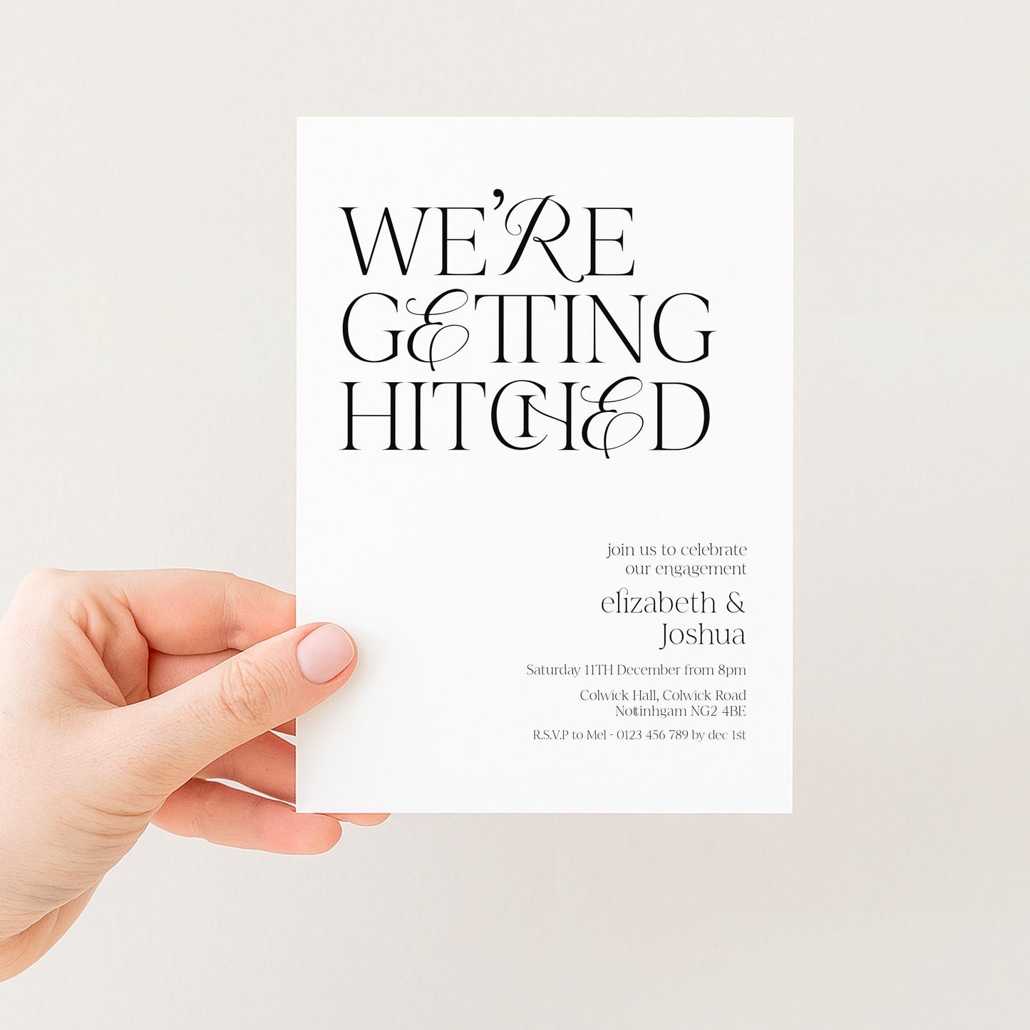a hand holding a white wedding invitation card with black text.