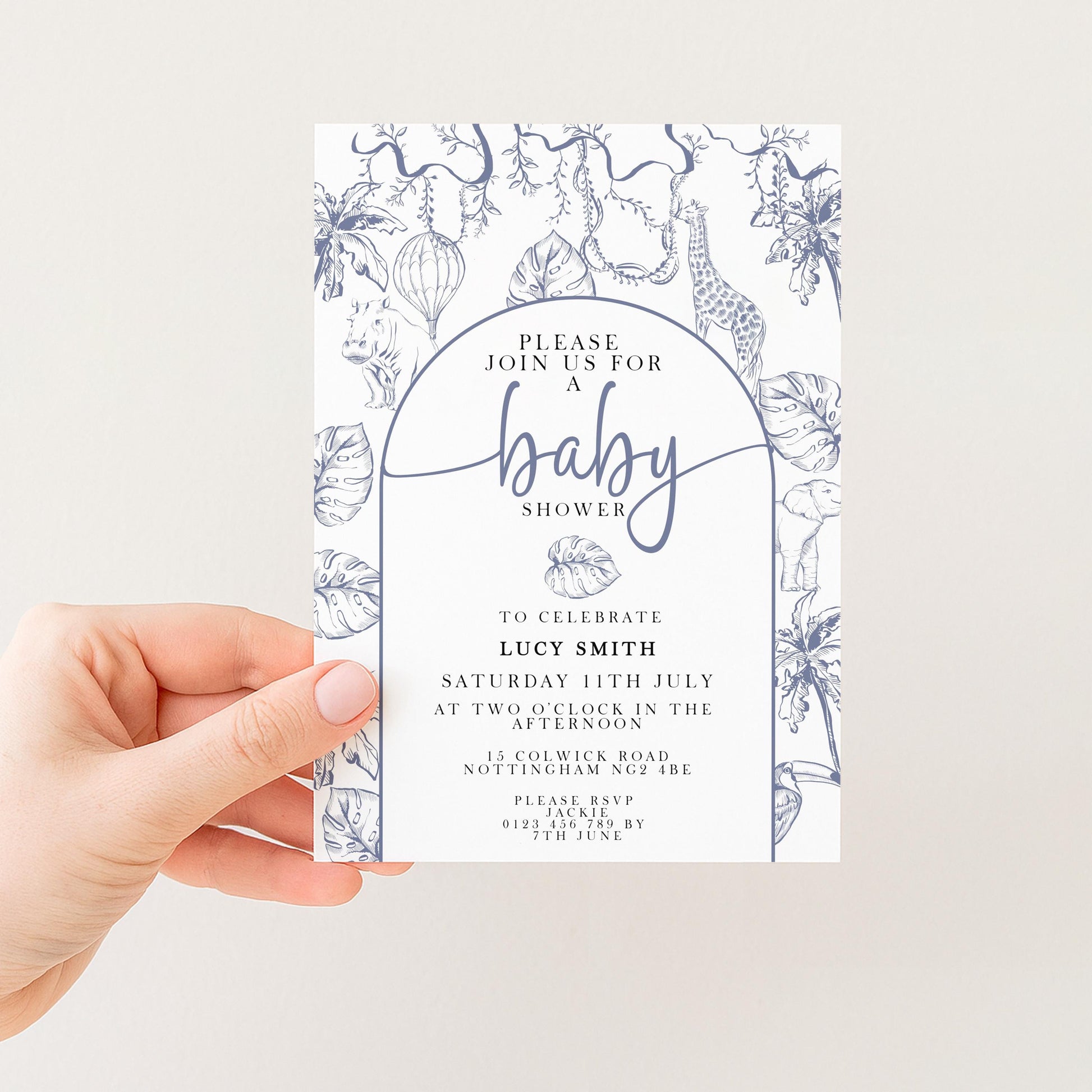 A hand holding a baby shower invitation with a floral and jungle-themed design.