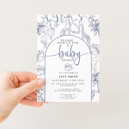A hand holding a baby shower invitation with a floral and jungle-themed design.