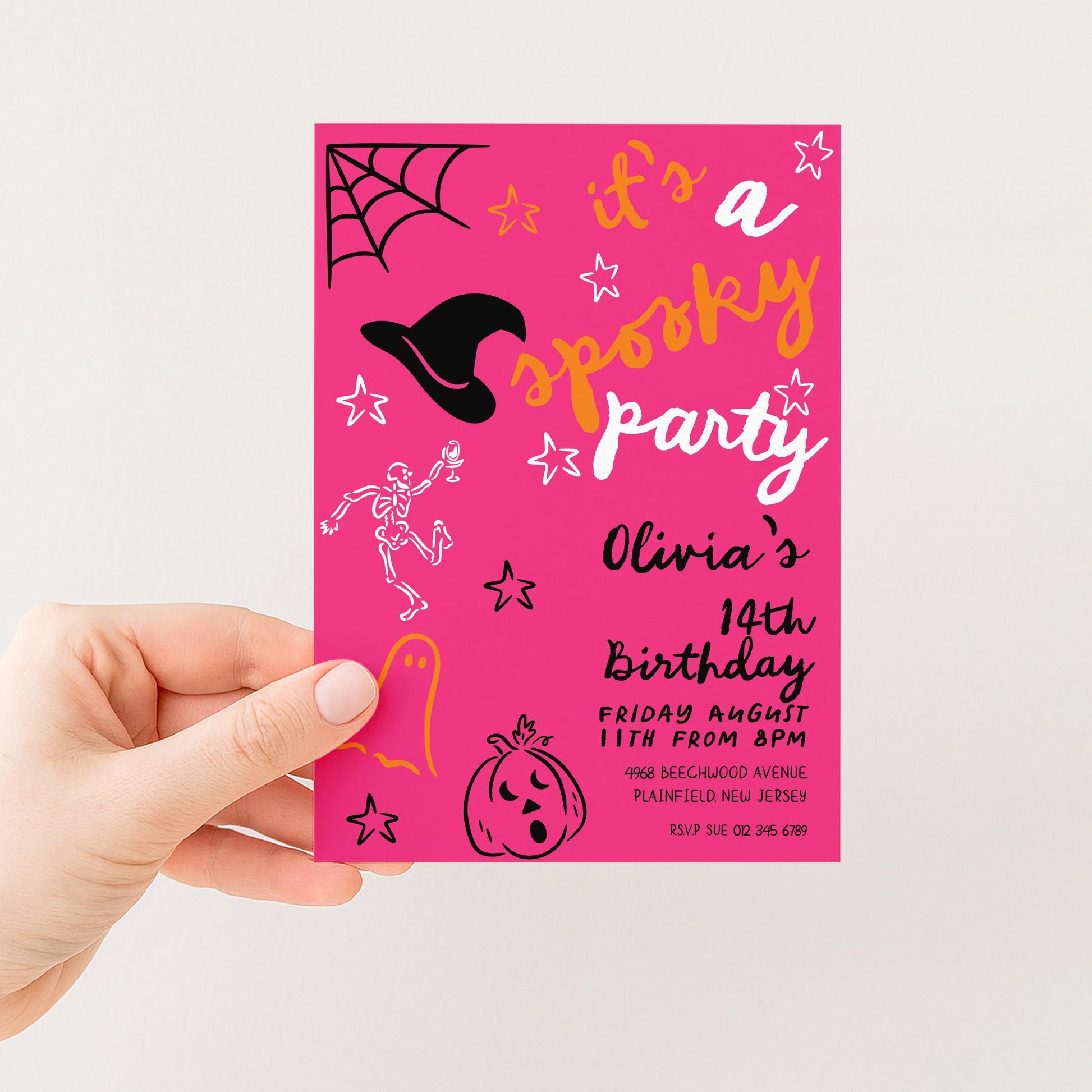 A hand holding a pink birthday party invitation with Halloween-themed illustrations and text.