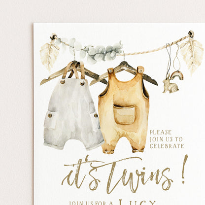 The image is a watercolor painting of baby clothes, including white onesies and yellow jumpsuits, hanging on a clothesline. The painting is accompanied by text inviting guests to a baby shower celebration.