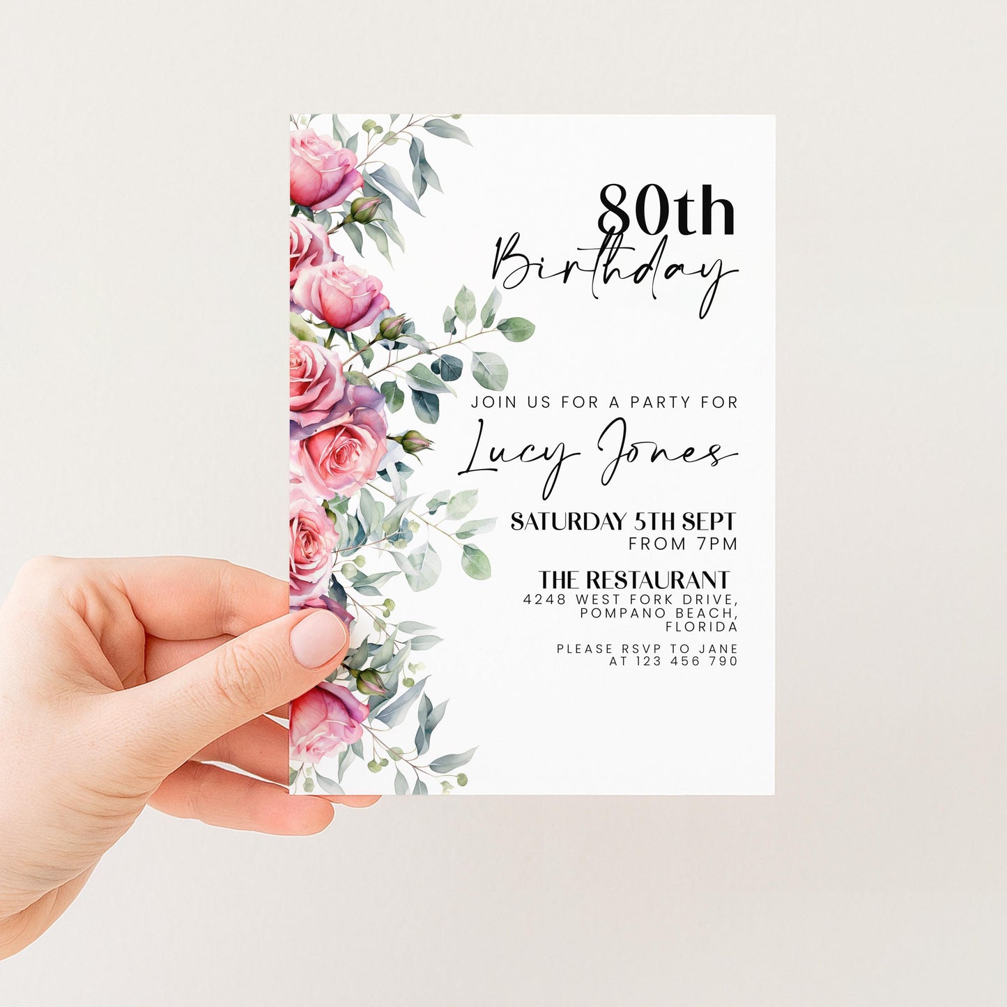 A hand holding a birthday invitation card with a floral design and text.