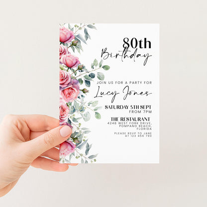 A hand holding a birthday invitation card with a floral design and text.