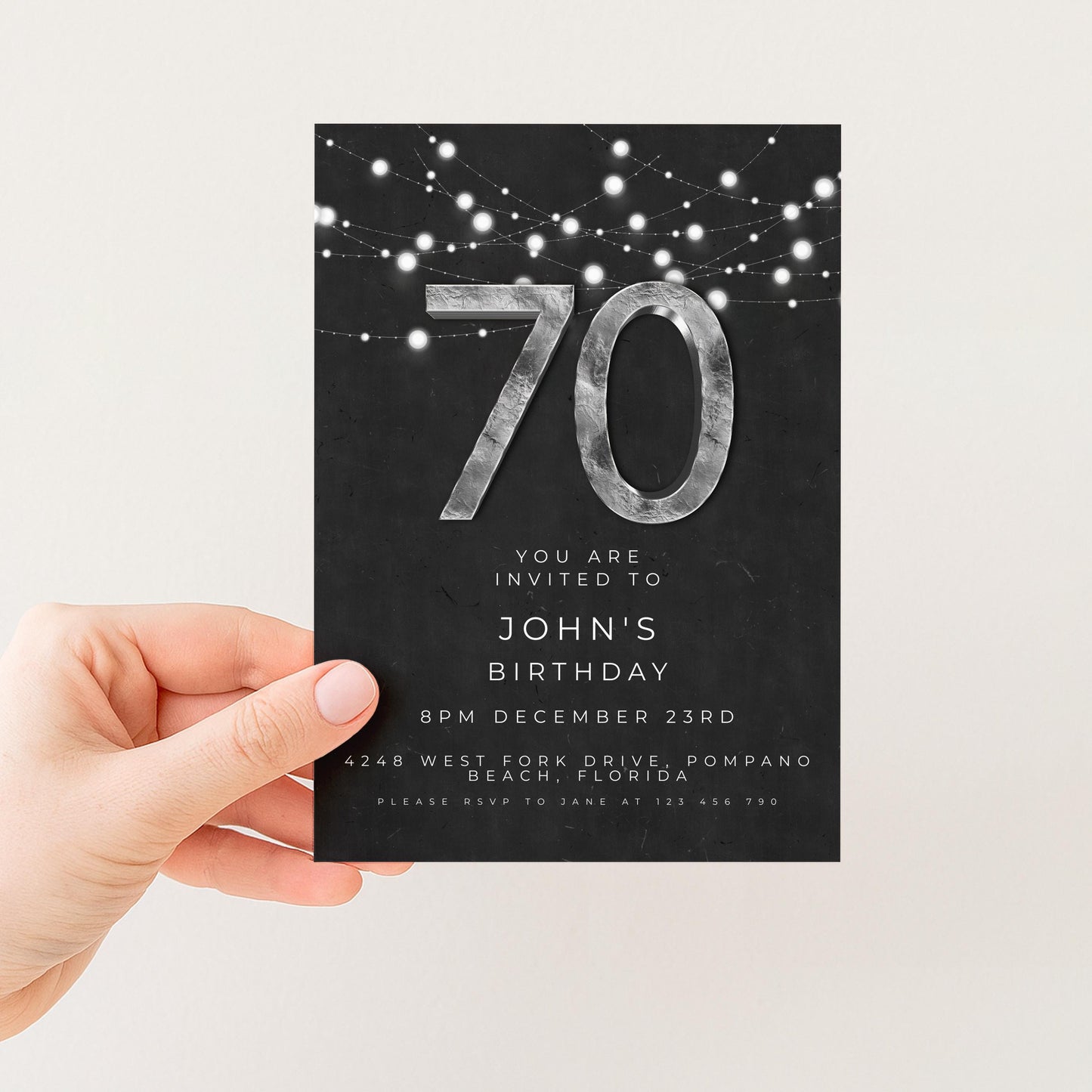 a person holding a black and white birthday invitation card with the number 70 on it.