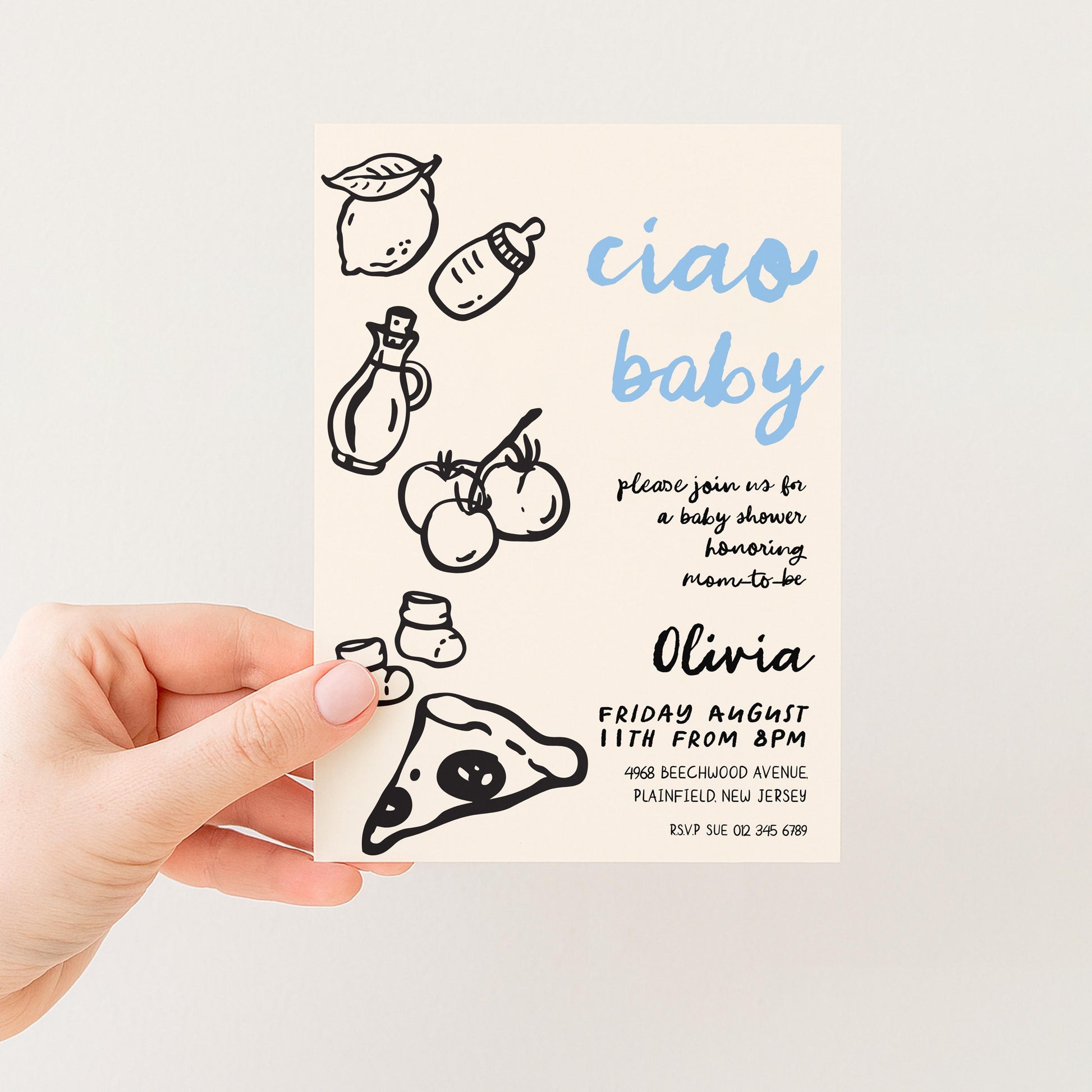 A hand holding a baby shower invitation card with various baby-related illustrations and text.