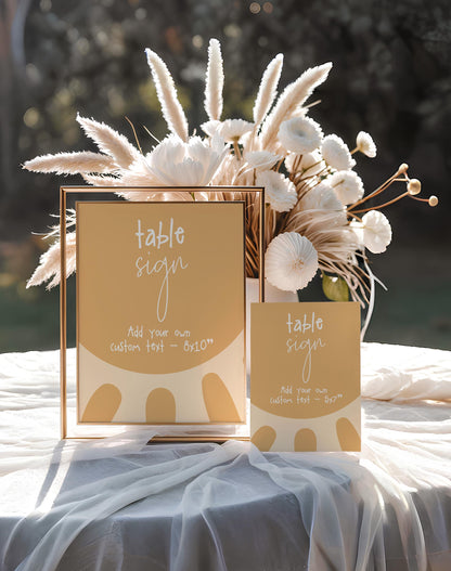 a table sign and a small card with a table sign design, placed on a table with a white tablecloth.