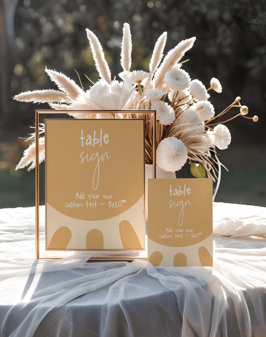a table sign and a small card with a table sign design, placed on a table with a white tablecloth.