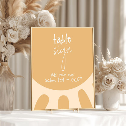 a table sign with a floral design, placed on a table next to a vase of white flowers.